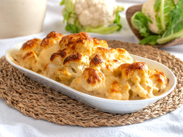 Soft pieces of cauliflower are enveloped in a crea...